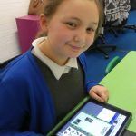 A child smiles as she writes a geography fact file on ainforest Habitats on a tablet using Purple Mash