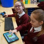 2 children smile to camera as they work together to design a 3D game.