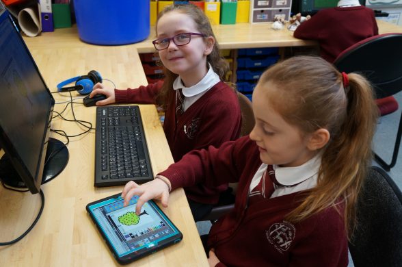 2 children smile to camera as they work together to design a 3D game.