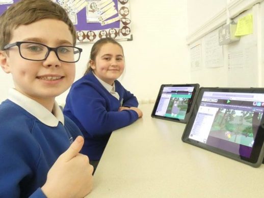 Two children smile to camera after completing a coding challenge in 2Code, the coding tool in Purple Mash